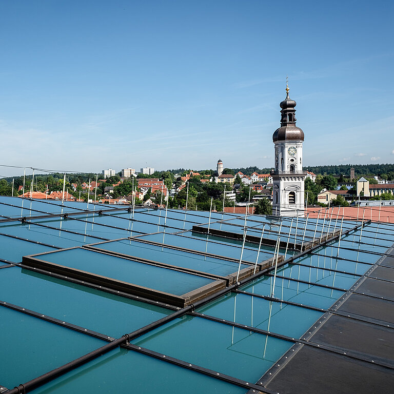 Blick auf ein Glasdach von außen. Im Hintergrund ein Kirchturm