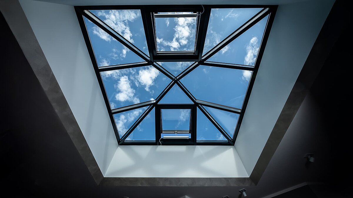 Blick von innen auf eine moderne Glaspyramide im Einfamilienhaus in Wichmannsdorf, die den Himmel und Wolken zeigt.