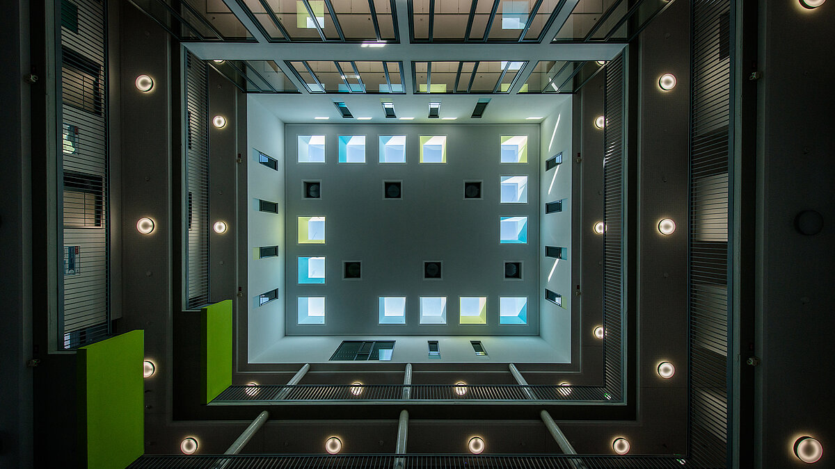 Blick von unten über mehrere Stockwerke zum Dach, das mit 14 quadratischen Flachdach Fenstern Licht ins Gebäude bringt