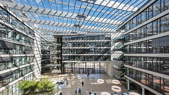 Großzügiges Atrium des FGS Campus mit Glasdach, modernen Bürogebäuden, Lichteinfall und Sitzbereichen.
