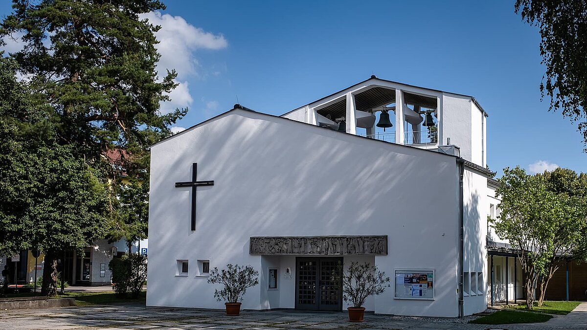 Moderne Pauluskirche in Traunreut mit weißer Fassade, großem Kreuz und Glockenturm.
