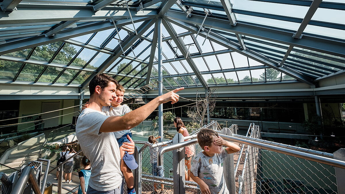 Vater mit Kindern unter der PR60-Glaskonstruktion im Zoo Neuwied, zeigt auf eine Attraktion.