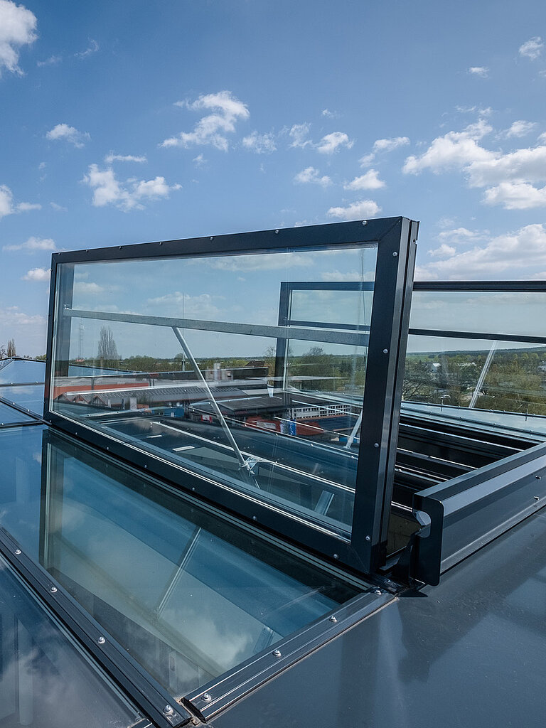 Geöffnetes RWA-Fenster mit transparenter Verglasung auf Flachdach zur natürlichen Rauch- und Wärmeabführung