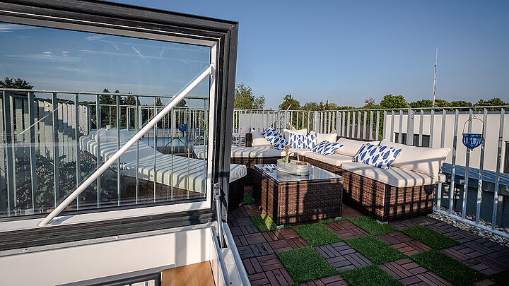 Moderne Dachterrasse mit Glasluke, Lounge-Möbeln und grüner Bodenverkleidung.