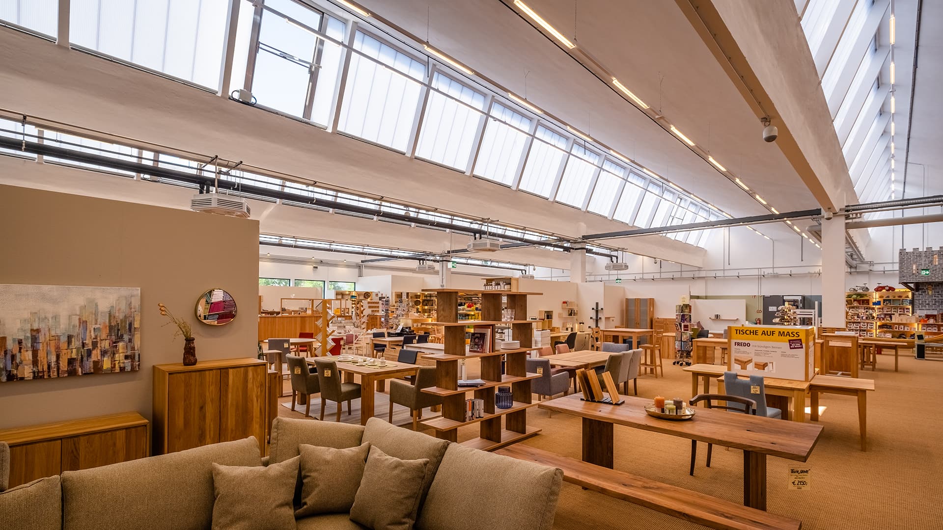 Innenansicht des alten Postbahnhofs Leipzig, umgestaltet als Möbelgeschäft mit modernem Design, natürlichen Lichtbändern und stilvollen Möbeln.