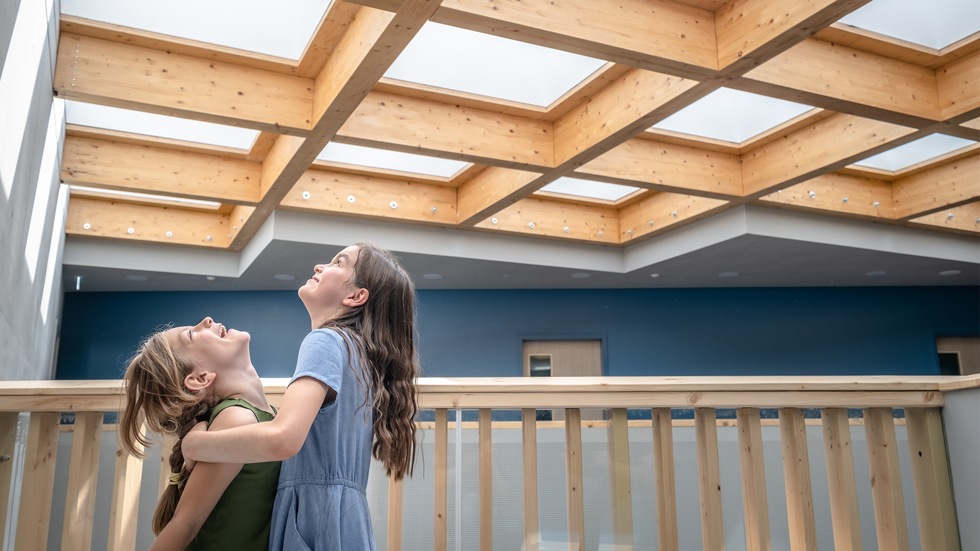 Zwei Mädchen stehen auf einem Holzbalkon und blicken zur Decke
